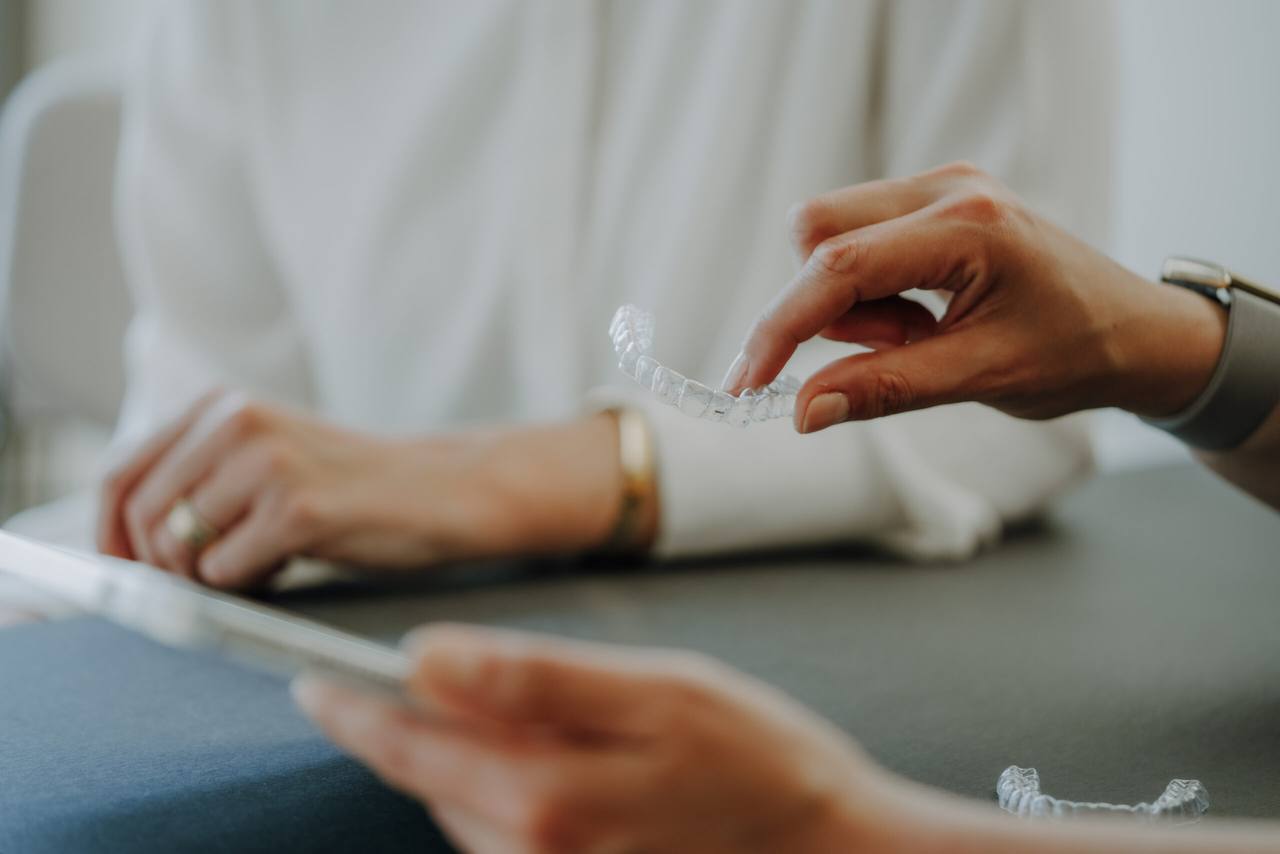 Transparente Aligner-Schiene in der Hand der Zahnärztin, im Hintergrund die Patientin am Beratungstisch