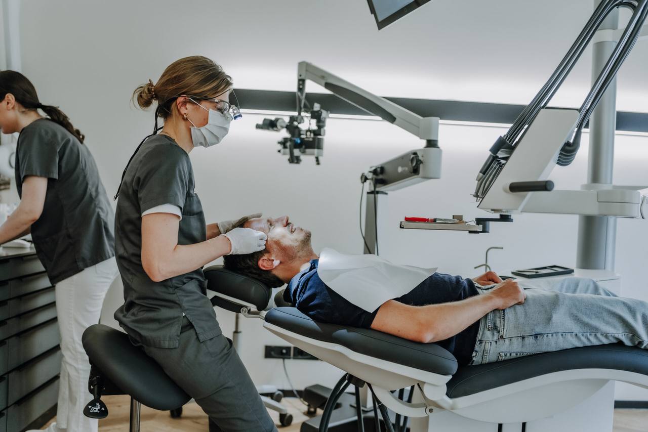 Zahnärztin untersucht einen entspannt lächelnden Patienten im hellen Behandlungszimmer