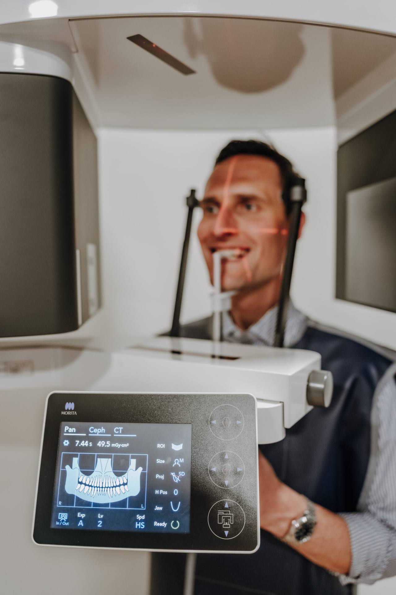 Bediendisplay des digitalen Röntgengeräts, dahinter lächelt ein Patient im Gerät