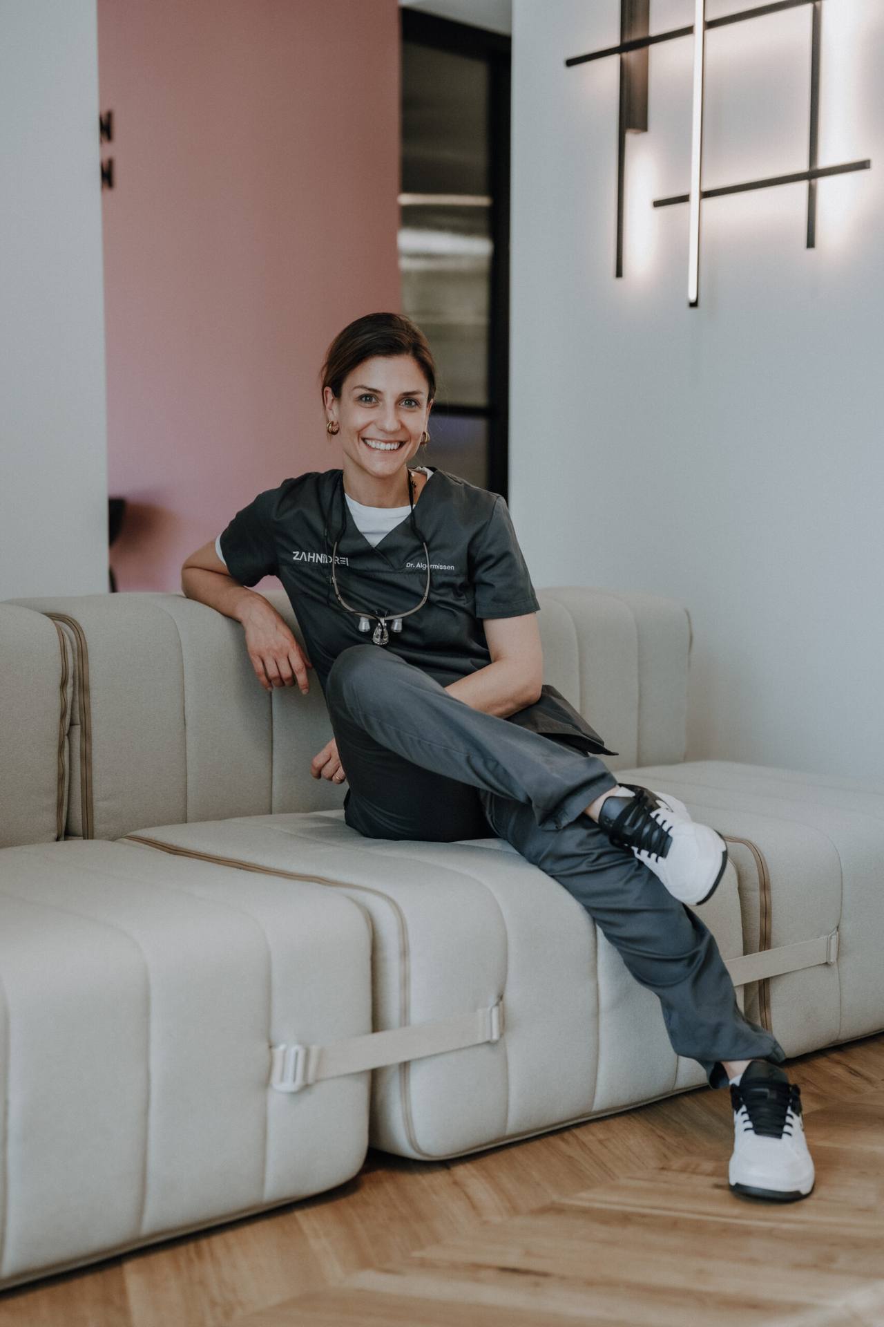 Dr. Teresa Algermissen sitzt entspannt auf dem hellen Sofa im Wartebereich von zahnhochdrei
