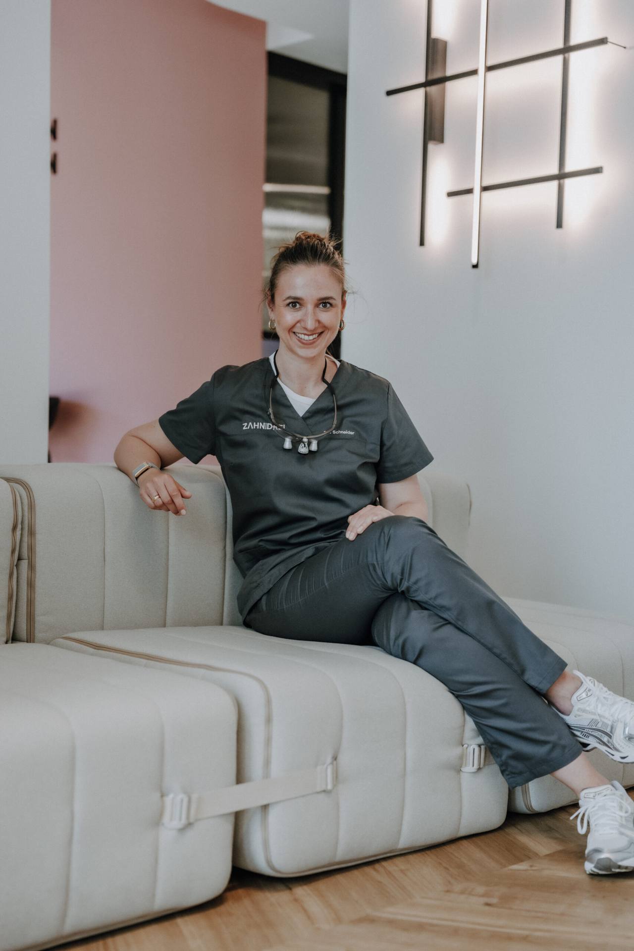 Franziska-Roberta Schneider sitzt frontal auf dem hellen Sofa im Wartebereich von zahnhochdrei