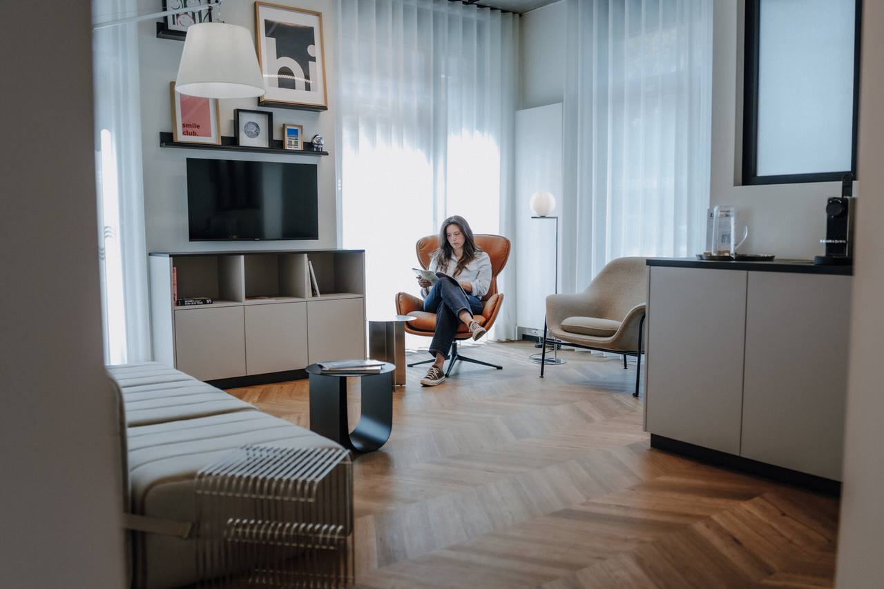 Loungeartiger Wartebereich mit Ledersessel, Kaffeestation und lesender Patientin