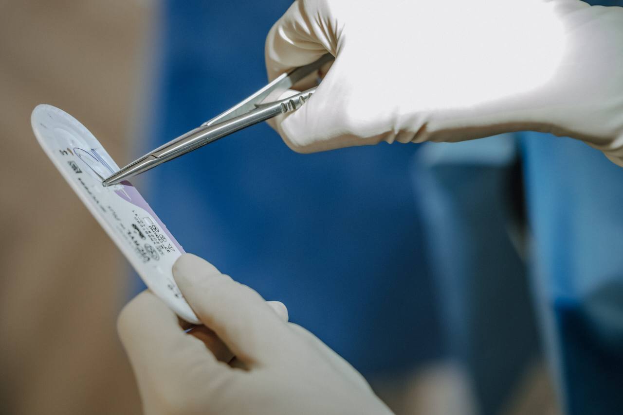 Sterile Handschuhe öffnen das Nahtmaterial mit dem Nadelhalter — Nahaufnahme aus der Oralchirurgie