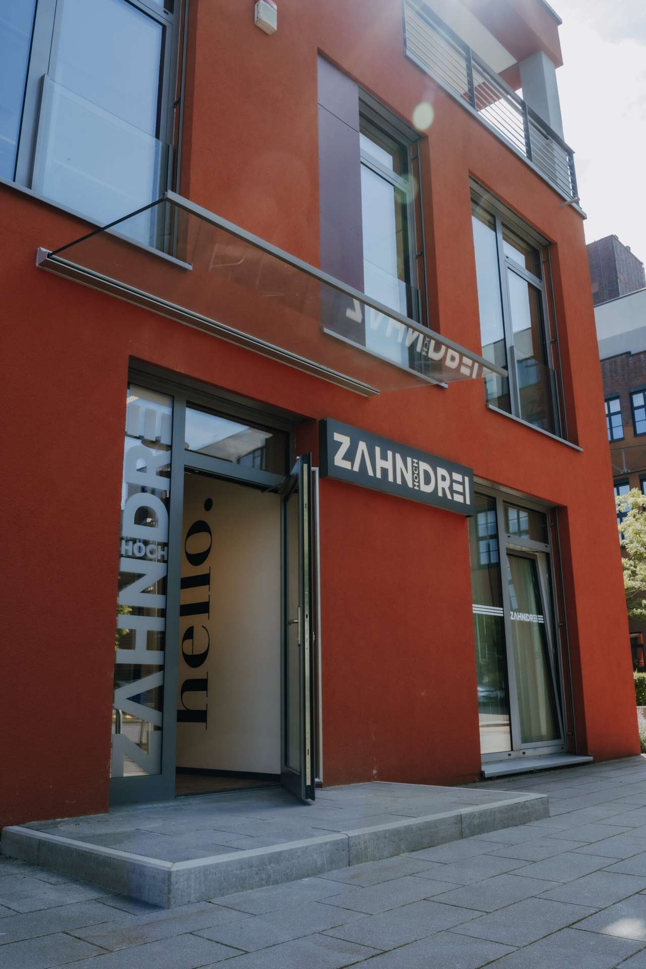 Geöffnete Eingangstür der Praxis mit hello-Schriftzug auf der Glasscheibe