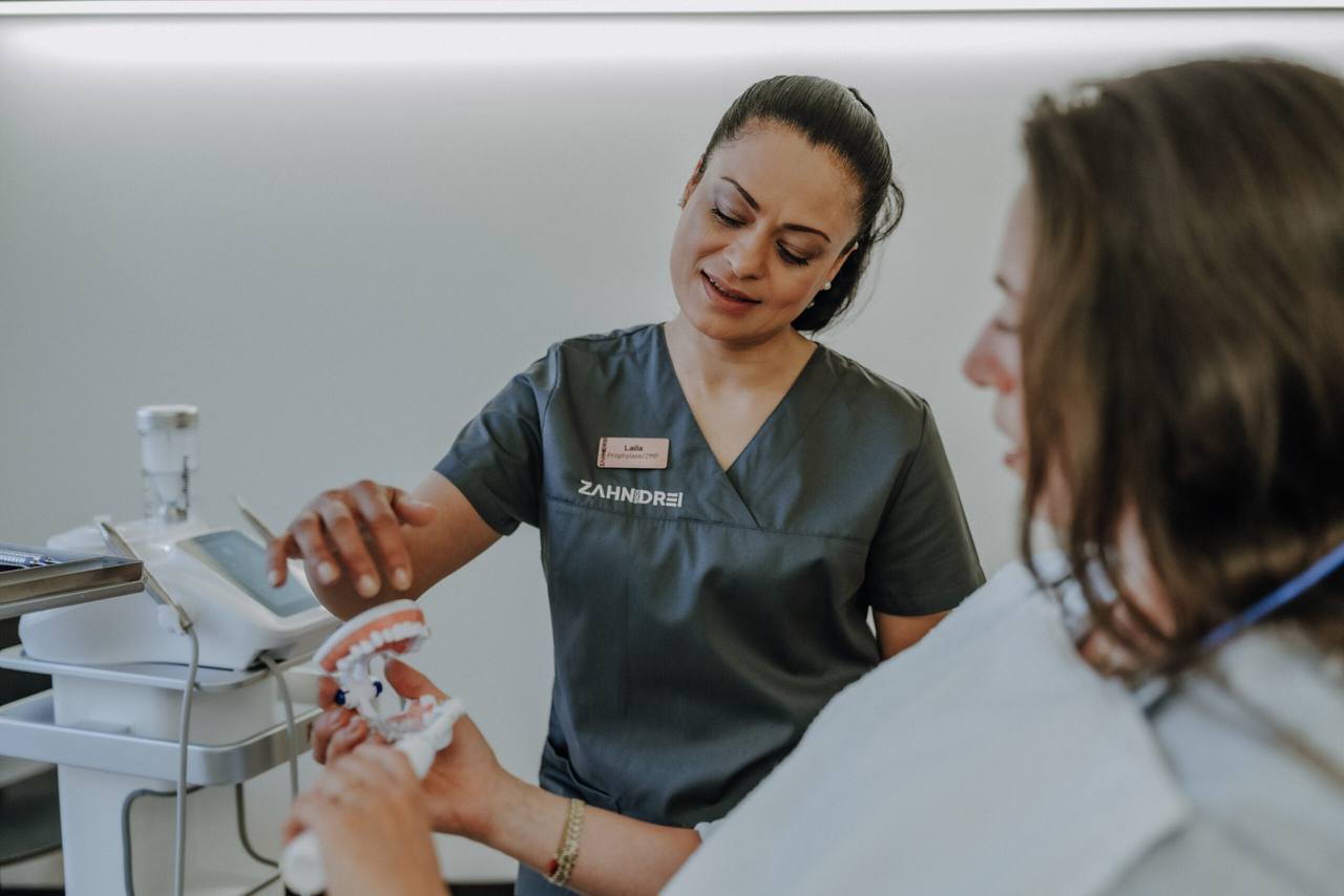 Prophylaxe-Expertin (ZMP) erklärt einer Patientin die richtige Putztechnik am Zahnmodell