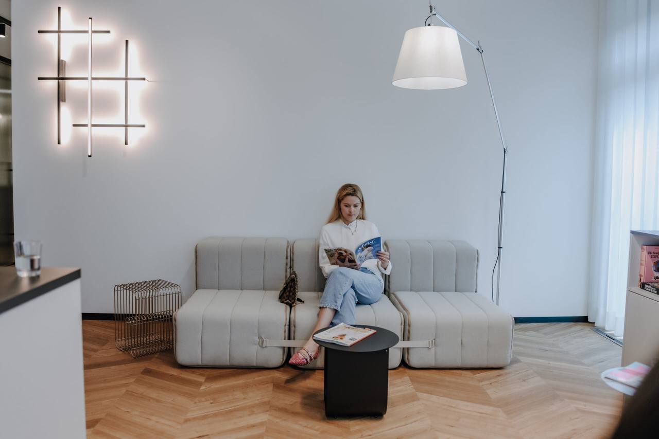 Patientin liest entspannt auf einem hellen Modulsofa im Wartebereich mit Lichtinstallation